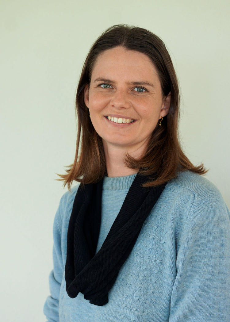 Woman wearing a blue sweater with a black scarf against a plain background