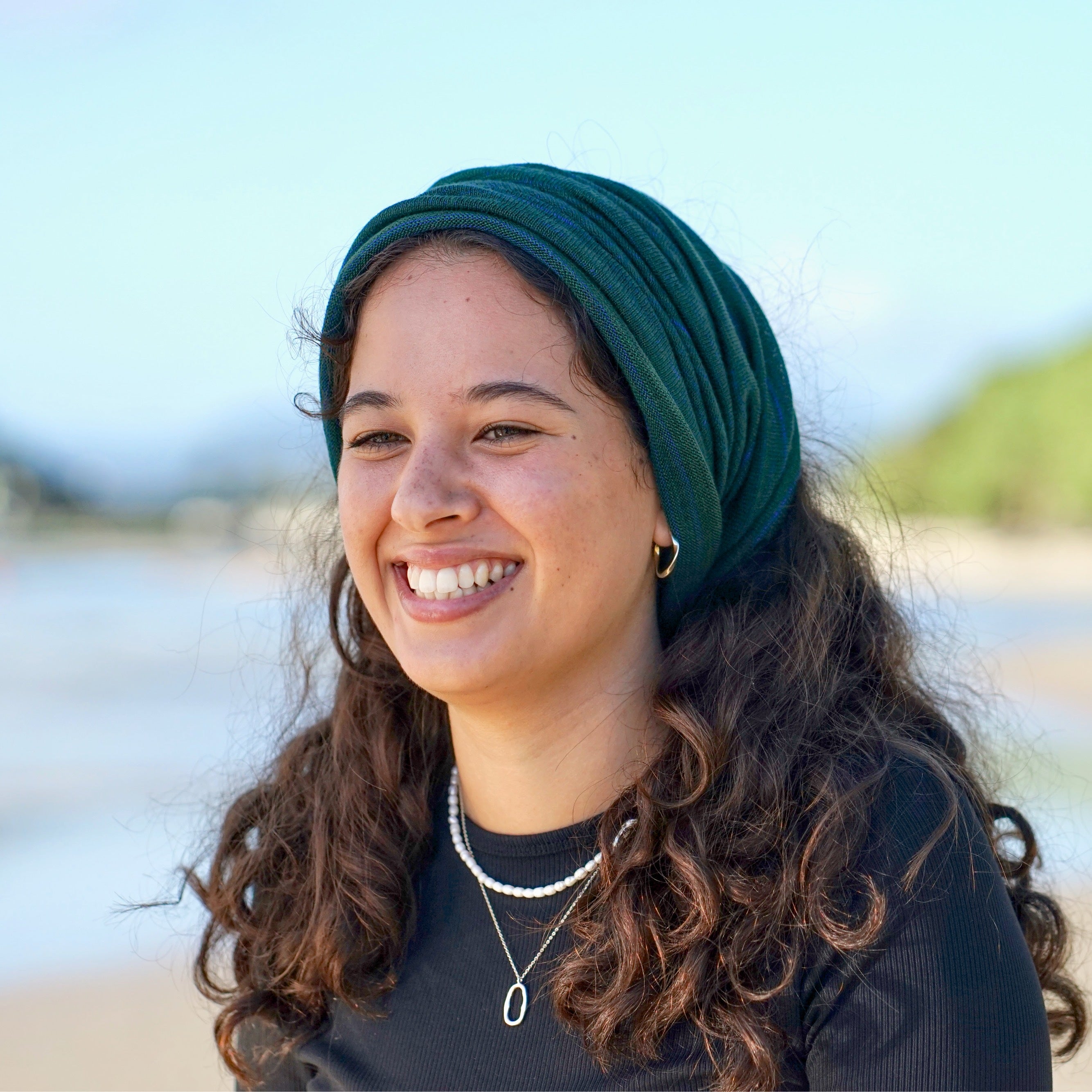 Woman wearing a green headscarf and black shirt on a beach