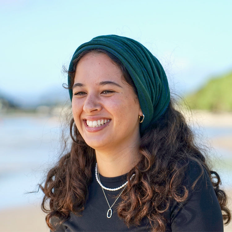 Woman wearing a green headscarf and black shirt on a beach